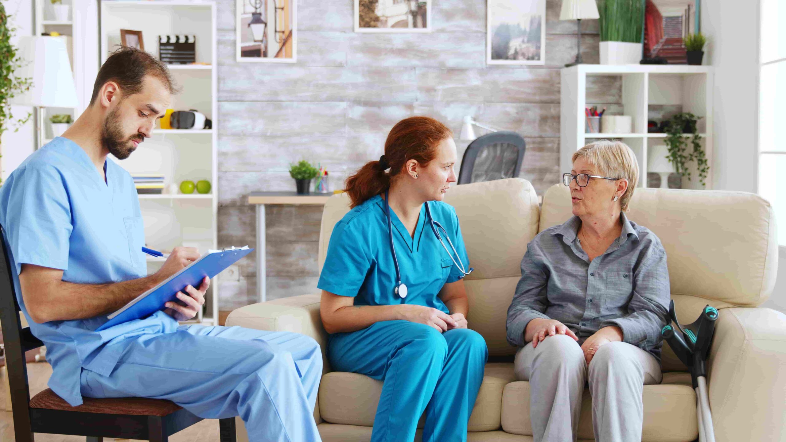 Male Assistant Taking Notes Clipboard While Female Doctor Is Talking With Senior Woman Nursing